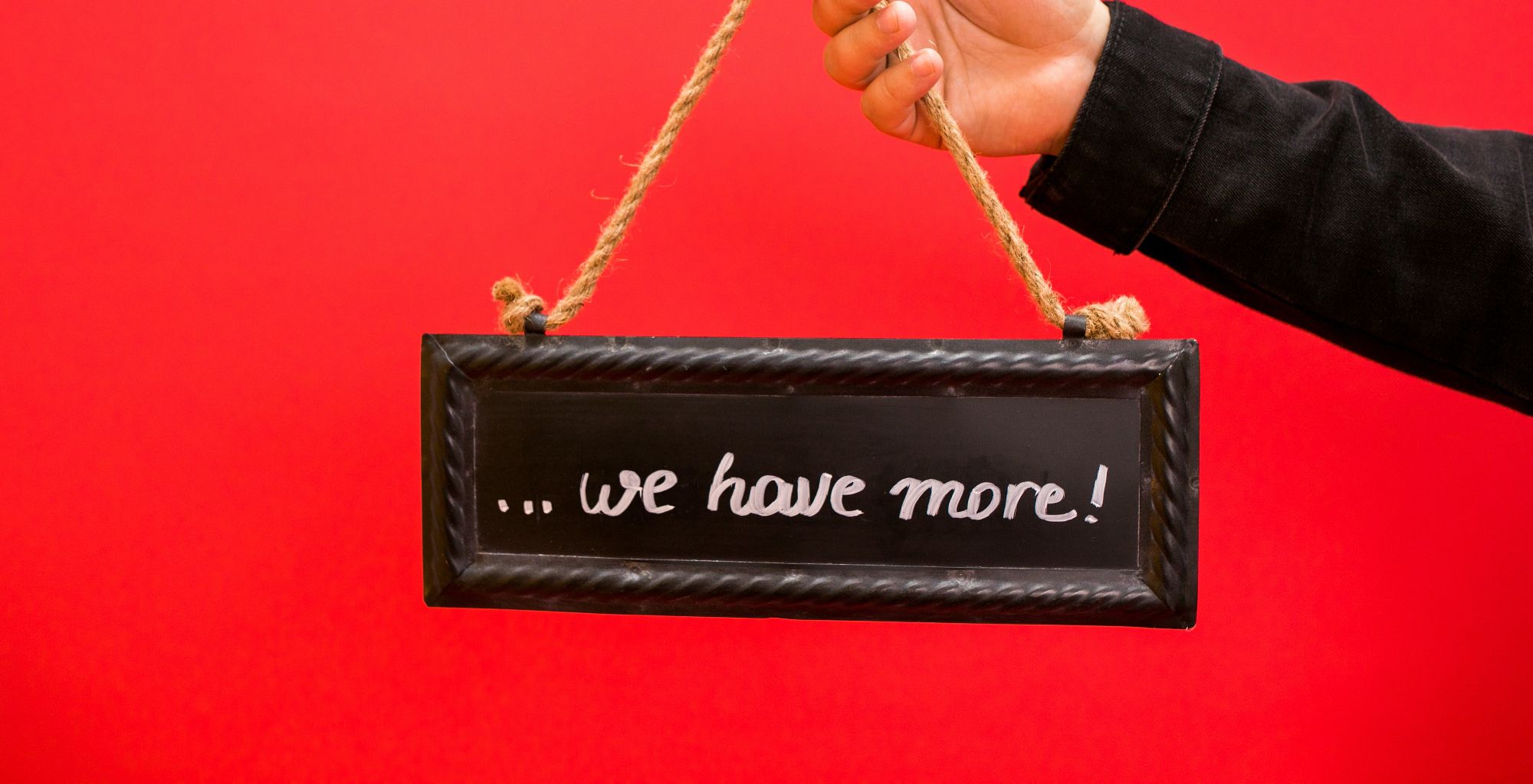 person holding 'we have more' sign in front of red background
