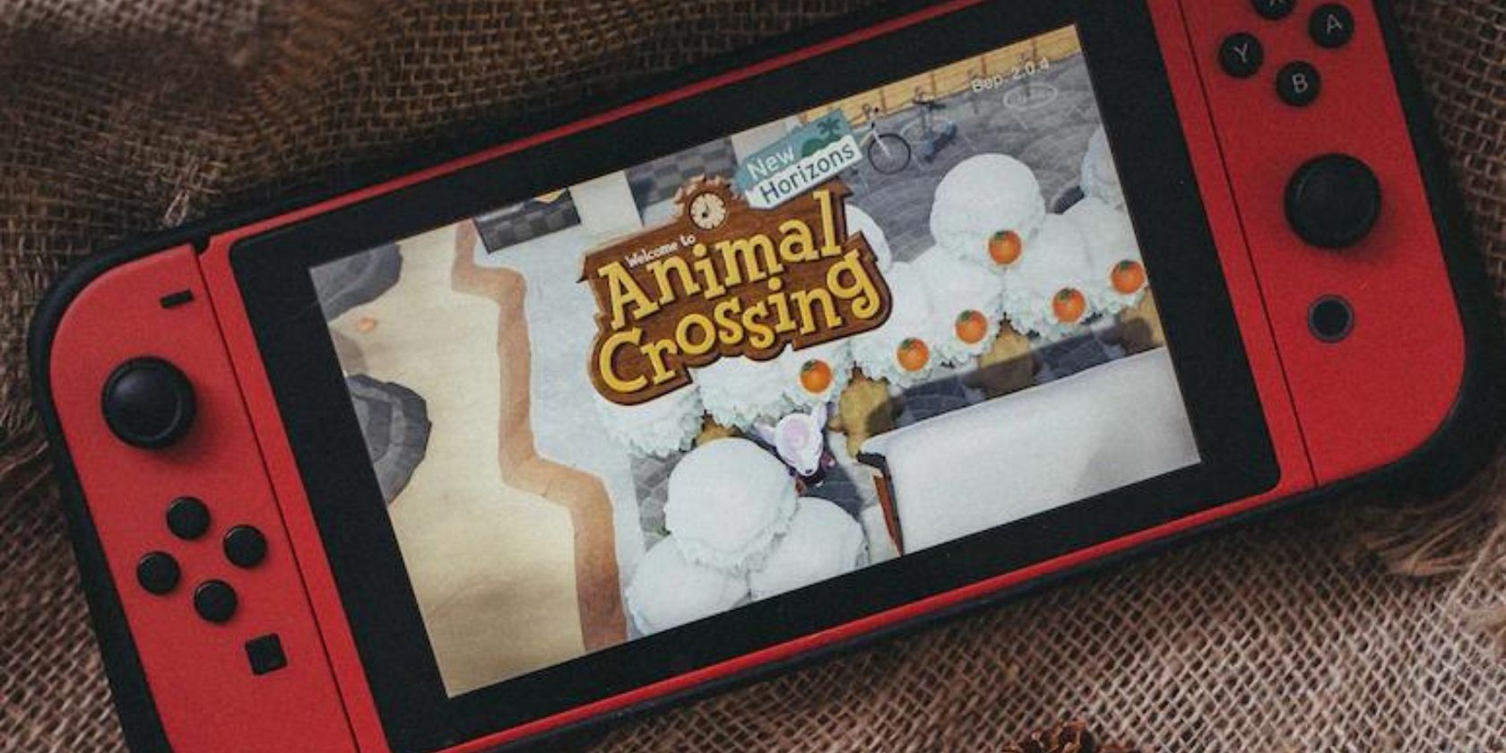 Красная консоль Nintendo Switch с запущенной Animal Crossing на фоне ткани