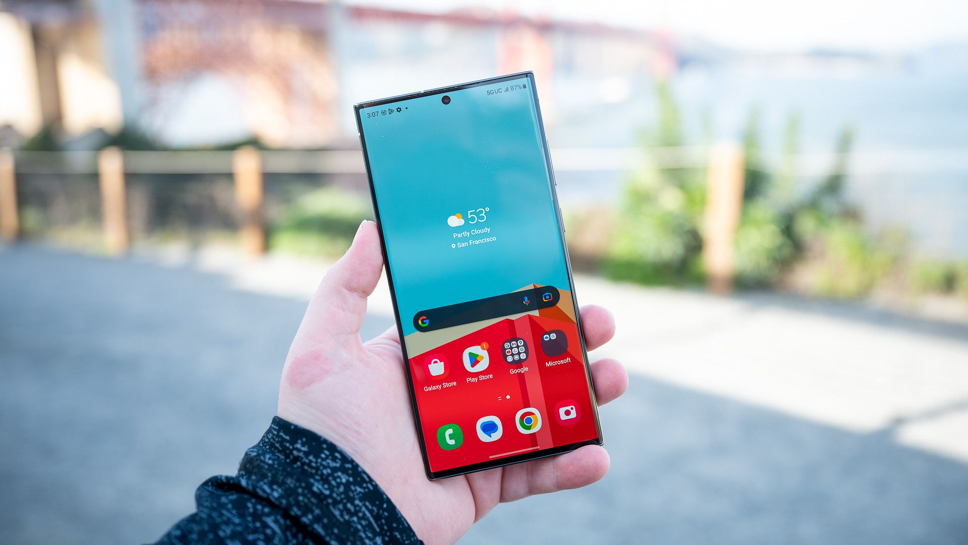 Человек держит Samsung Galaxy S23 Ultra с виджетом погоды на экране.