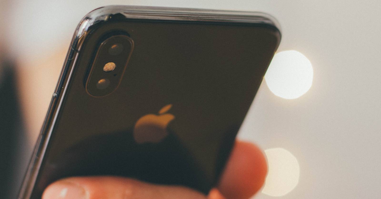 iPhone в руке — пальцы нажимают на заднюю панель