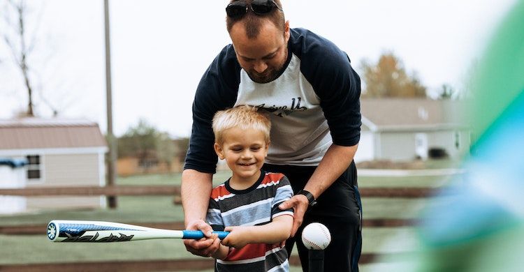 отец учит сына играть в бейсбол на улице
