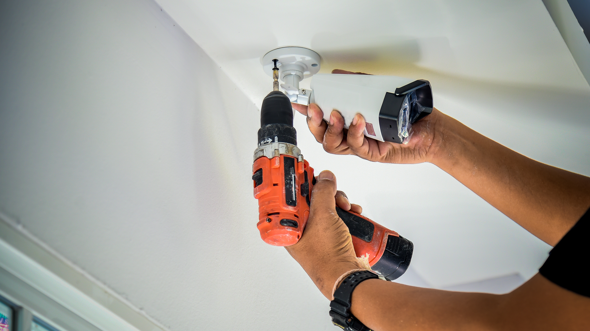 Мужчина устанавливает камеру наблюдения на потолке