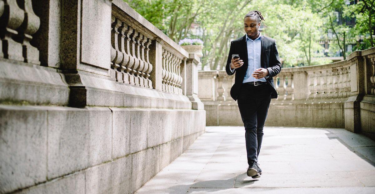 Человек в деловой одежде идет, глядя в телефон.