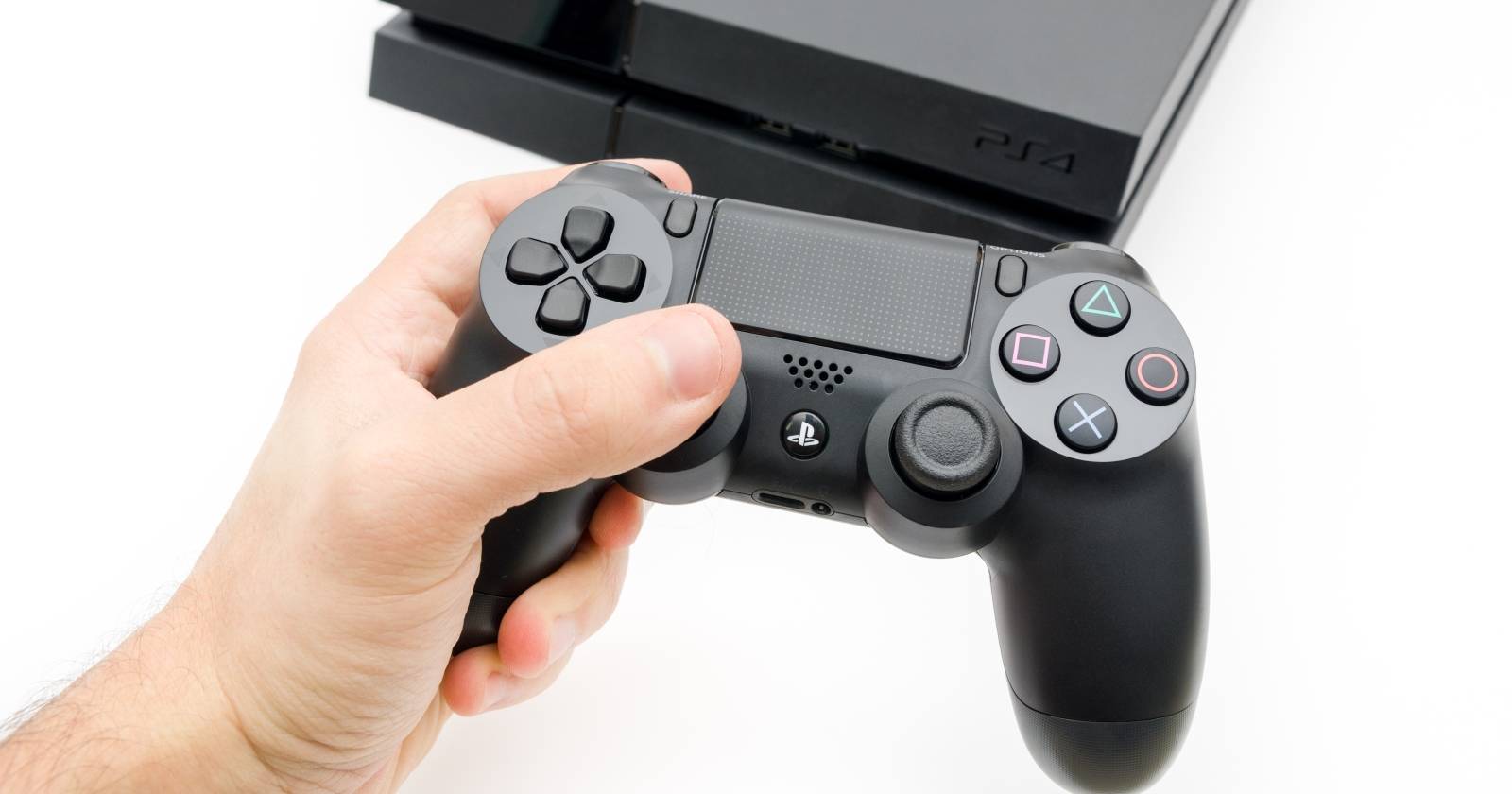Рука держит контроллер PS4 на фоне консоли PS4