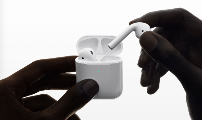 Пара белых беспроводных наушников и зарядная станция рядом с iPhone