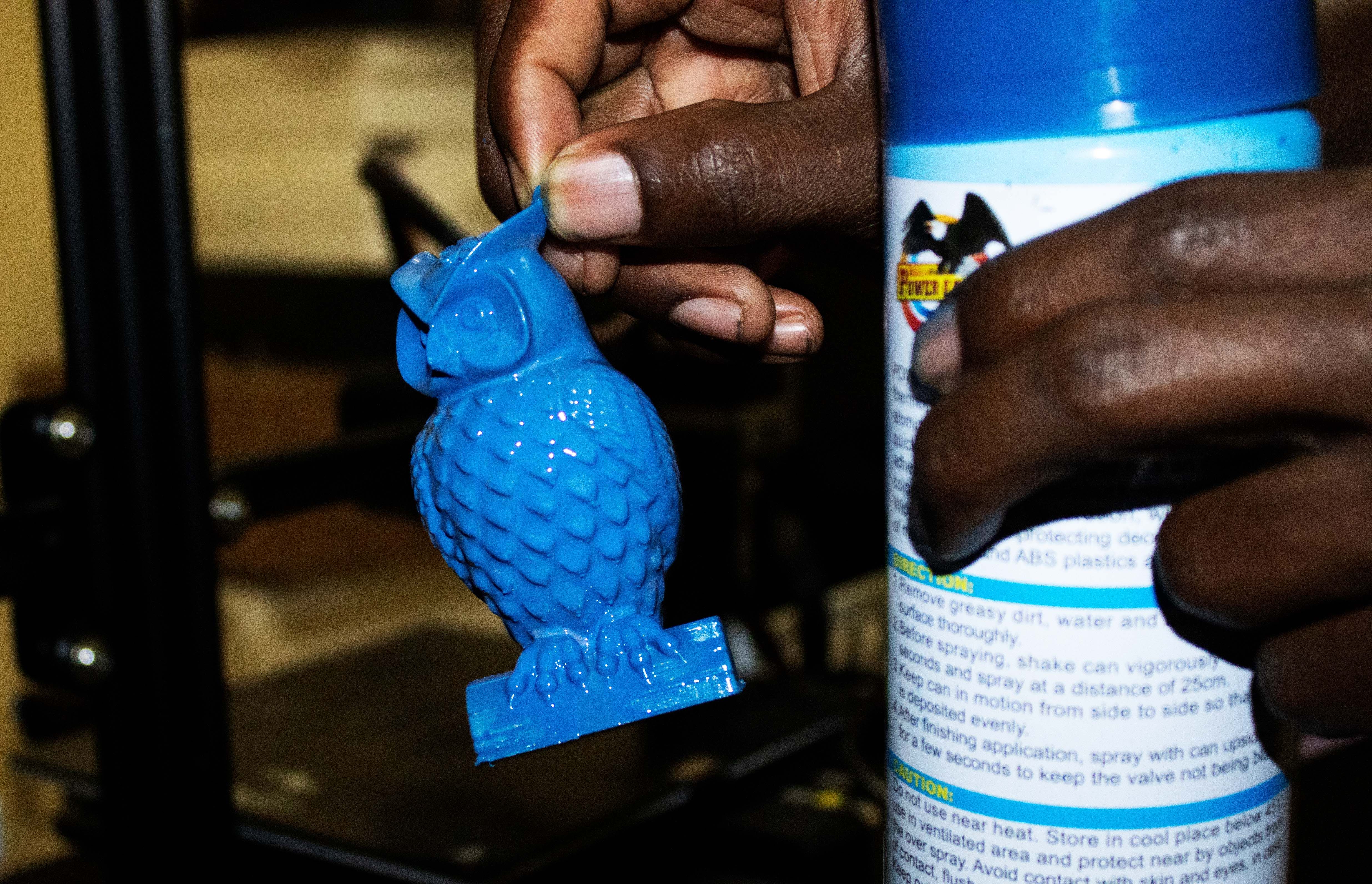Рука держит синюю 3D-модель совы и баллон краски