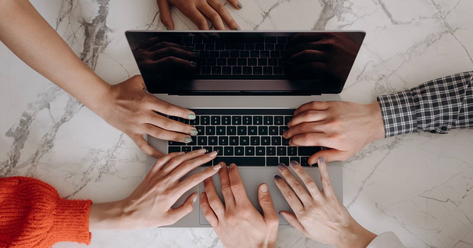 Несколько рук на клавиатуре MacBook, касающиеся разных клавиш.