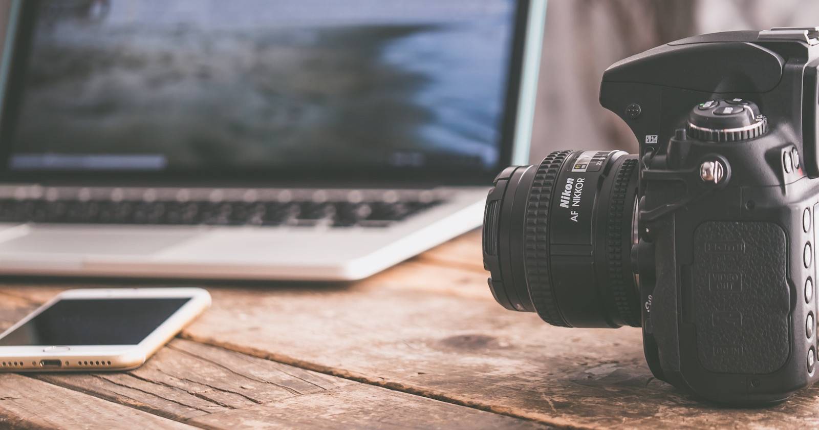 DSLR камера лежит рядом с ноутбуком и смартфоном на столе.