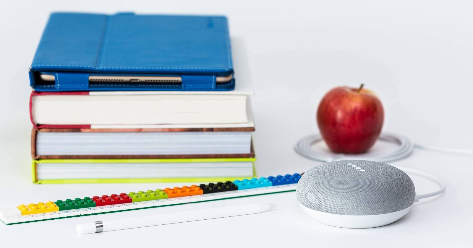 Серый Google Nest Mini рядом с книгами и яблоком