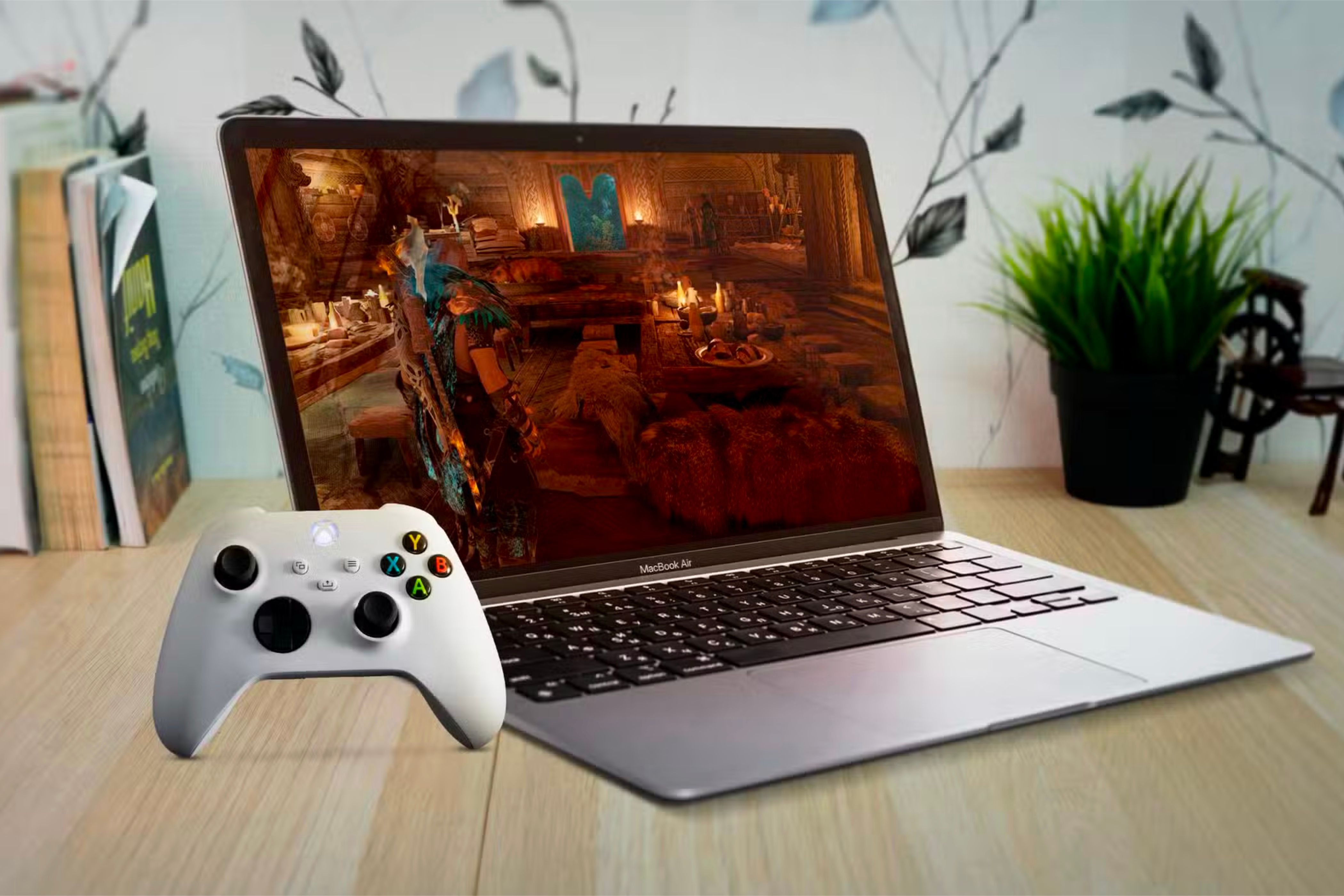 MacBook Air под деревянным столом, на экране игра и рядом контроллер Xbox