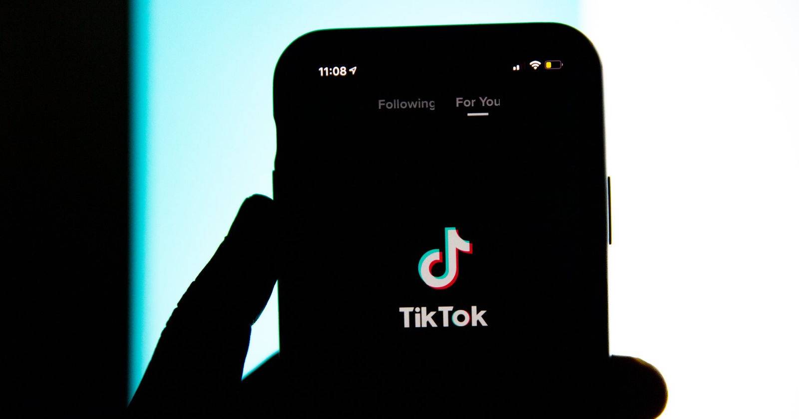 Человек в темной комнате держит телефон с открытым приложением TikTok
