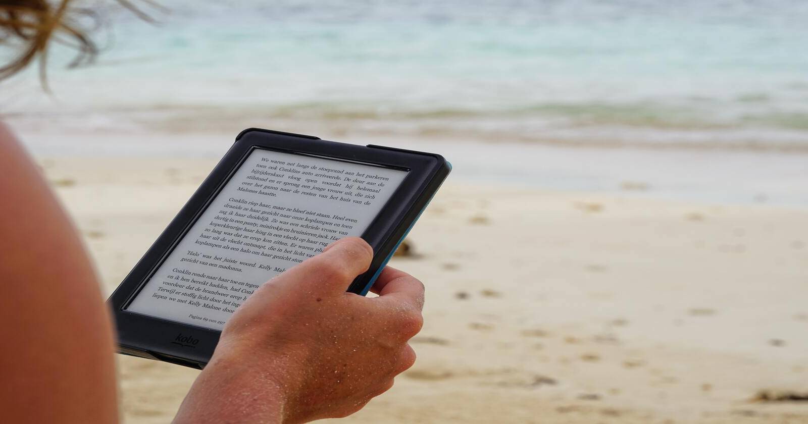 Человек держит Kindle на пляже