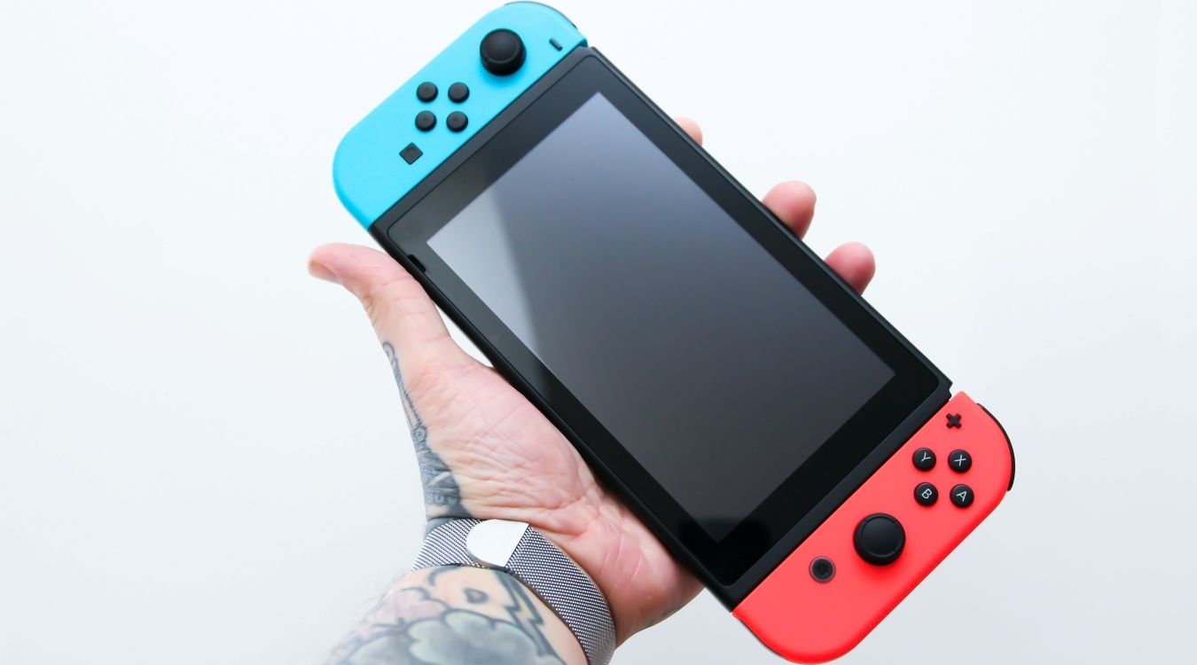 A photograph of a man holding up a Nintendo Switch in handheld mode