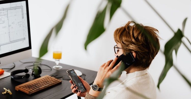 Изображение женщины за компьютером с телефоном в руках