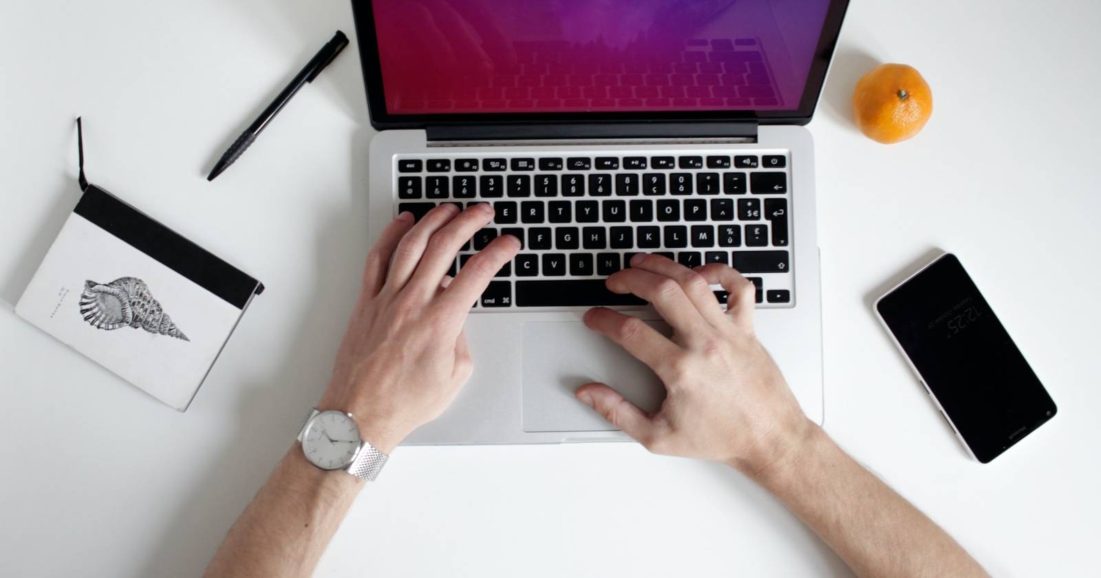 Печатание на ноутбуке с блокнотом, телефоном и фруктами рядом