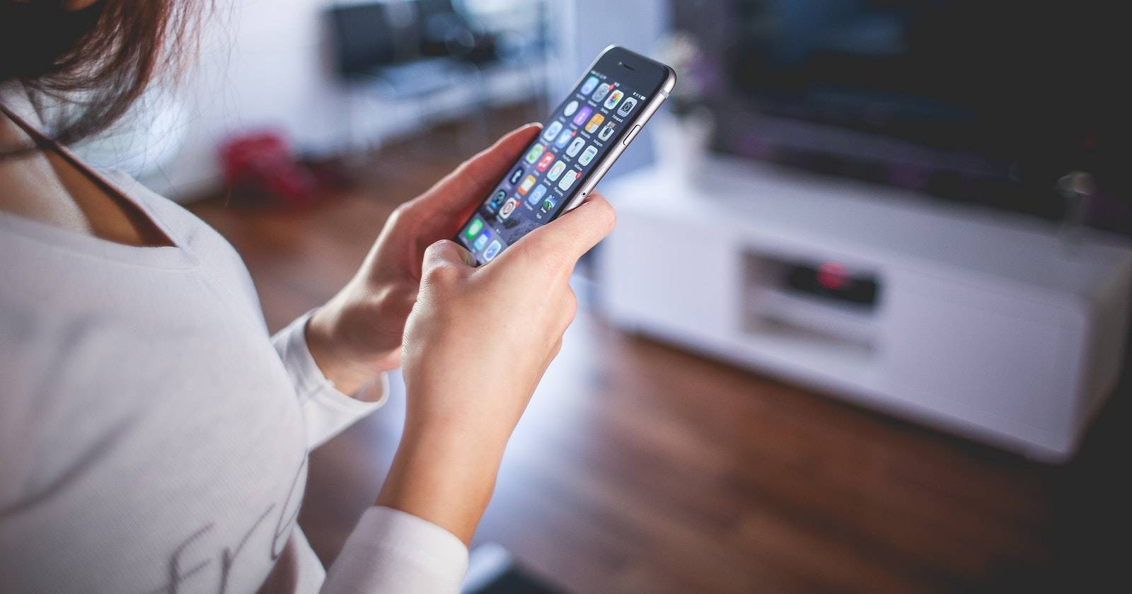 Женщина с iPhone на главном экране в серой футболке, на фоне телевизор