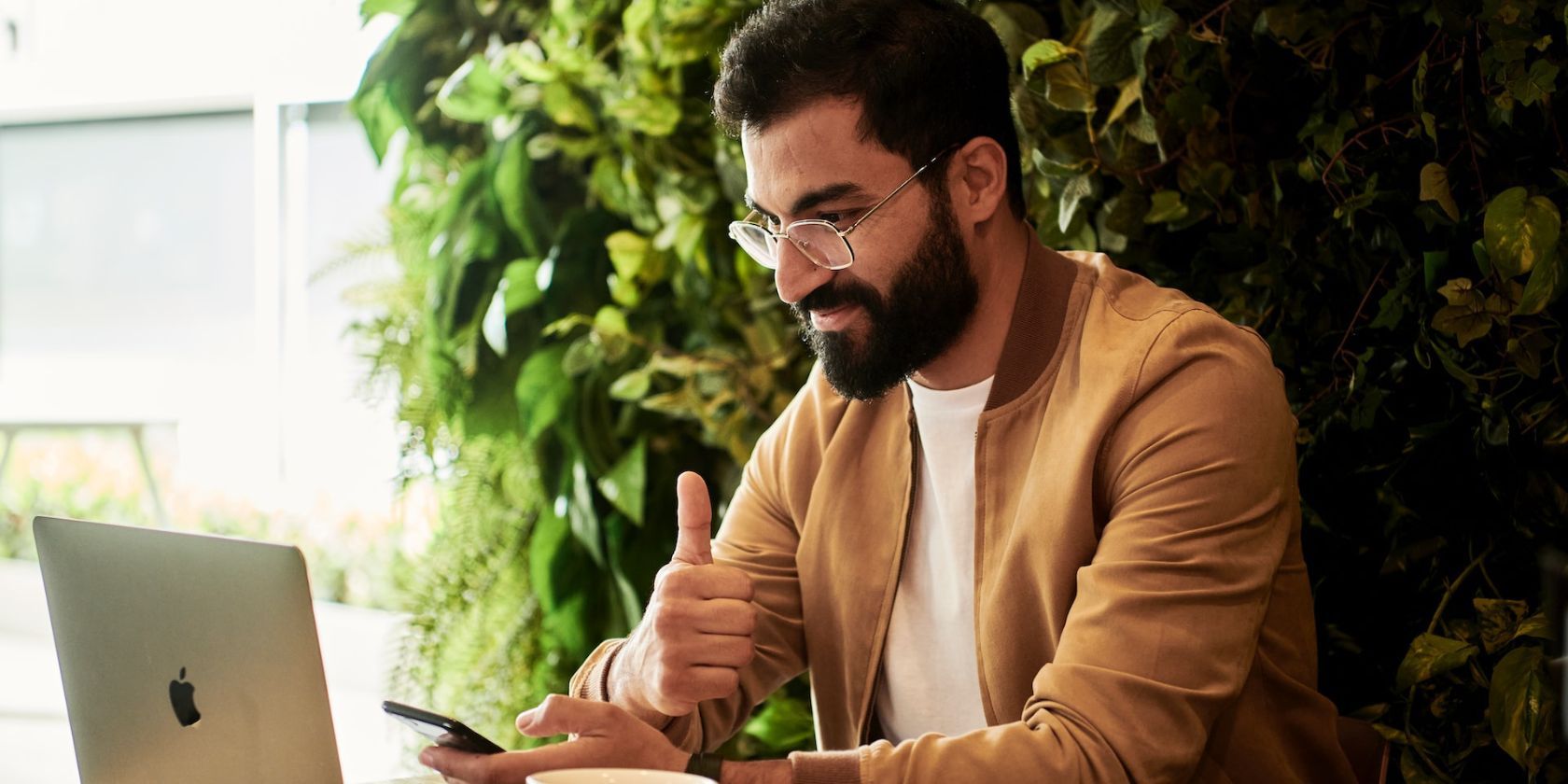 a man looking at his laptop and giving a thumbs up indicating satisfaction with his work.