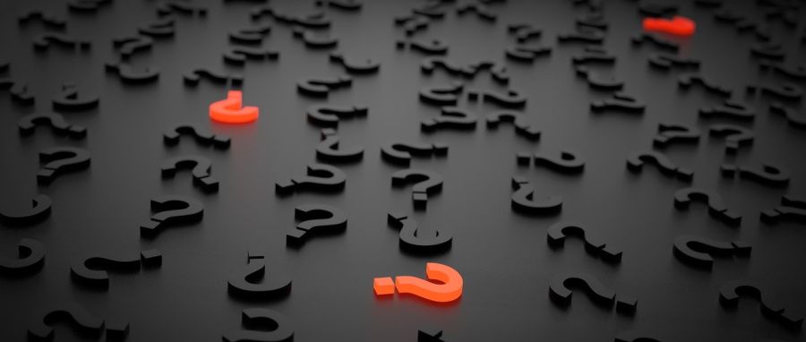 Множество тёмных трёхмерных знаков вопроса на полу; несколько ярко‑оранжевых выделяются на фоне