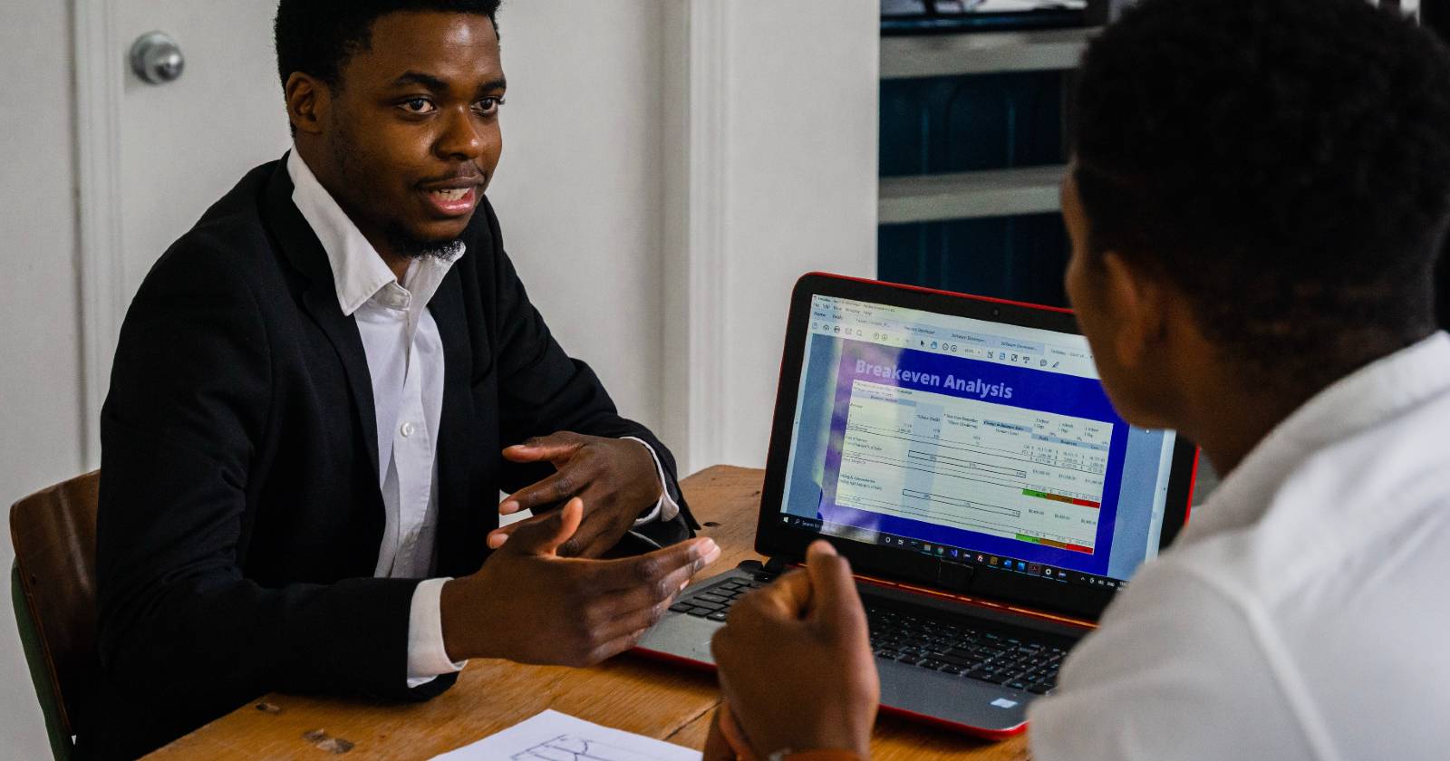 Мужчина в тёмном костюме беседует у ноутбука с коллегой