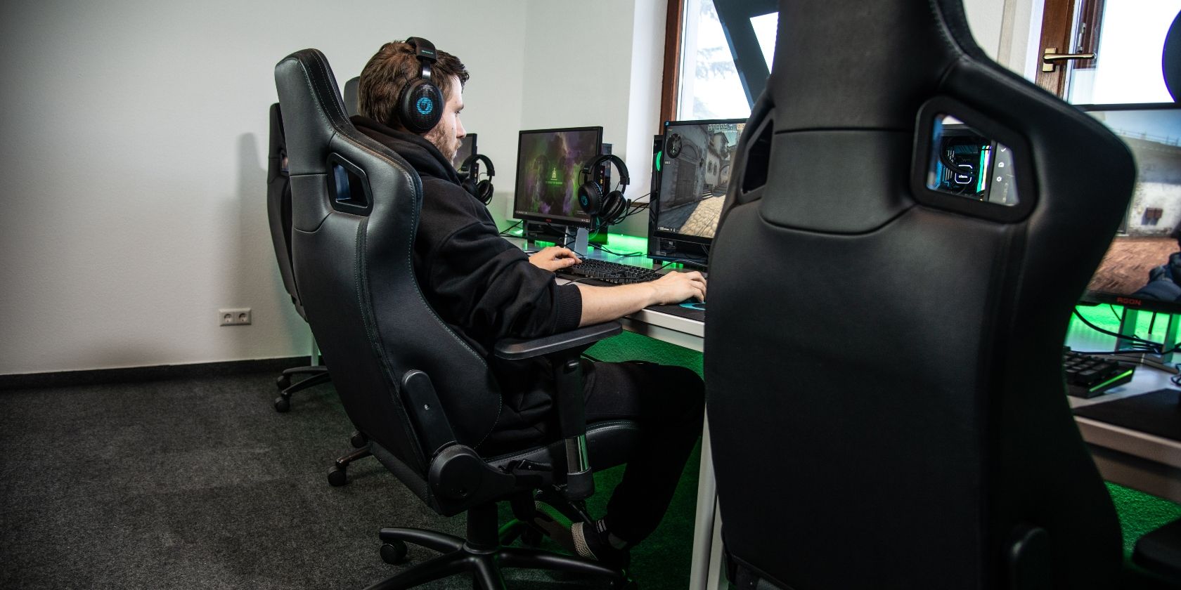 Стример в игровом кресле за столом с компьютерами