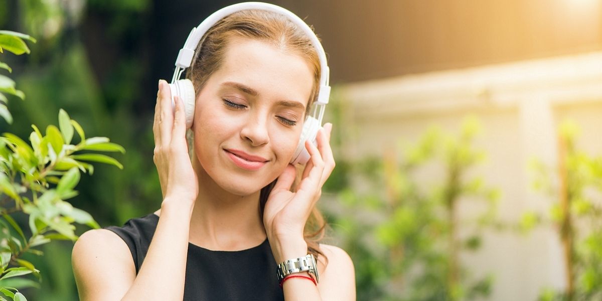 Женщина в черном платье держит белые наушники днем