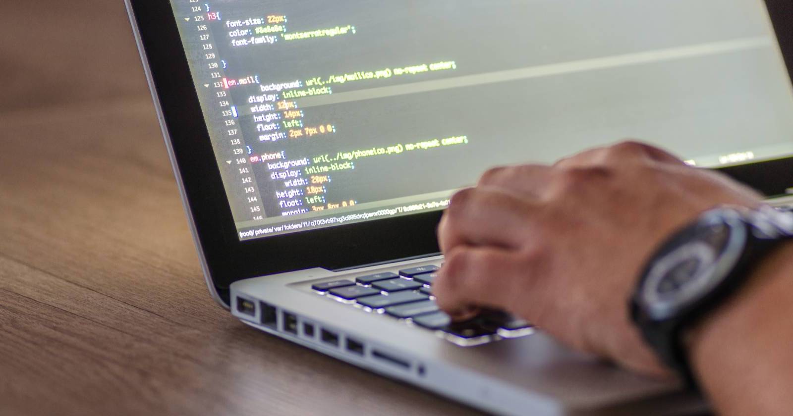 Крупный план руки, печатающей на клавиатуре ноутбука; на экране виден CSS‑код.