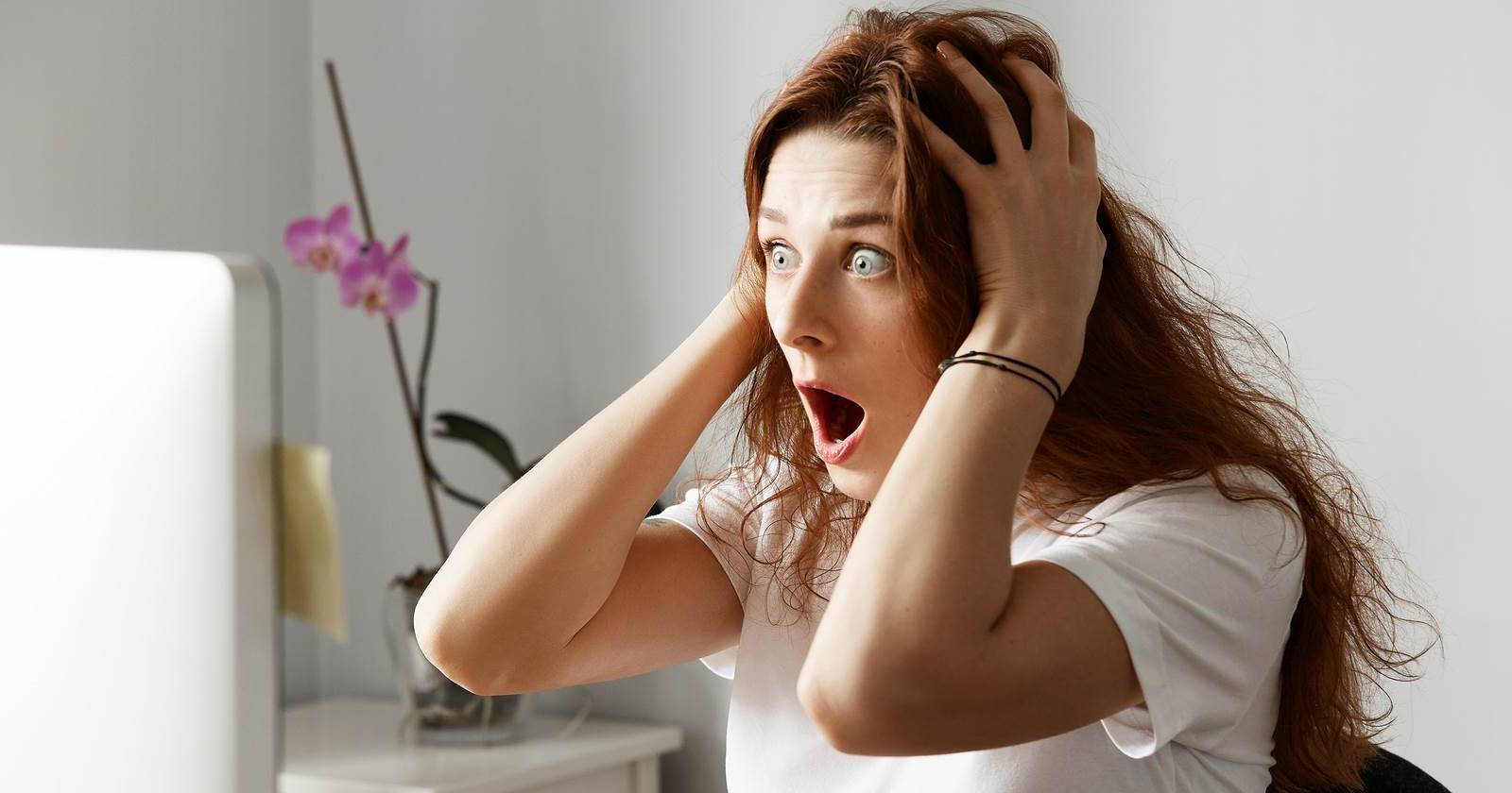 Женщина в шоке держится за голову, глядя на экран компьютера