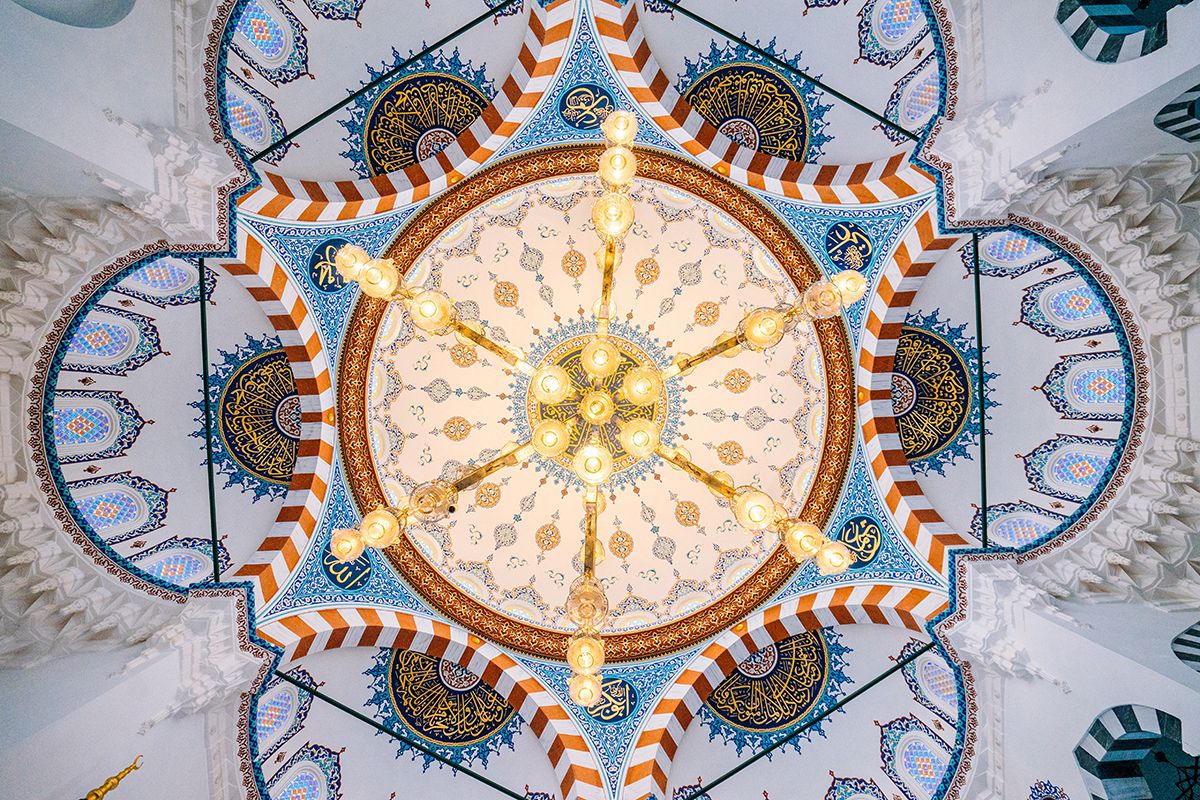 Photo look up from ground towards a decorated ceiling surrounding a chandelier.