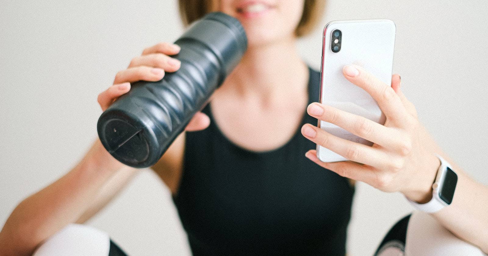 Человек в спортивной одежде держит iPhone в одной руке и бутылку воды в другой, на запястье Apple Watch