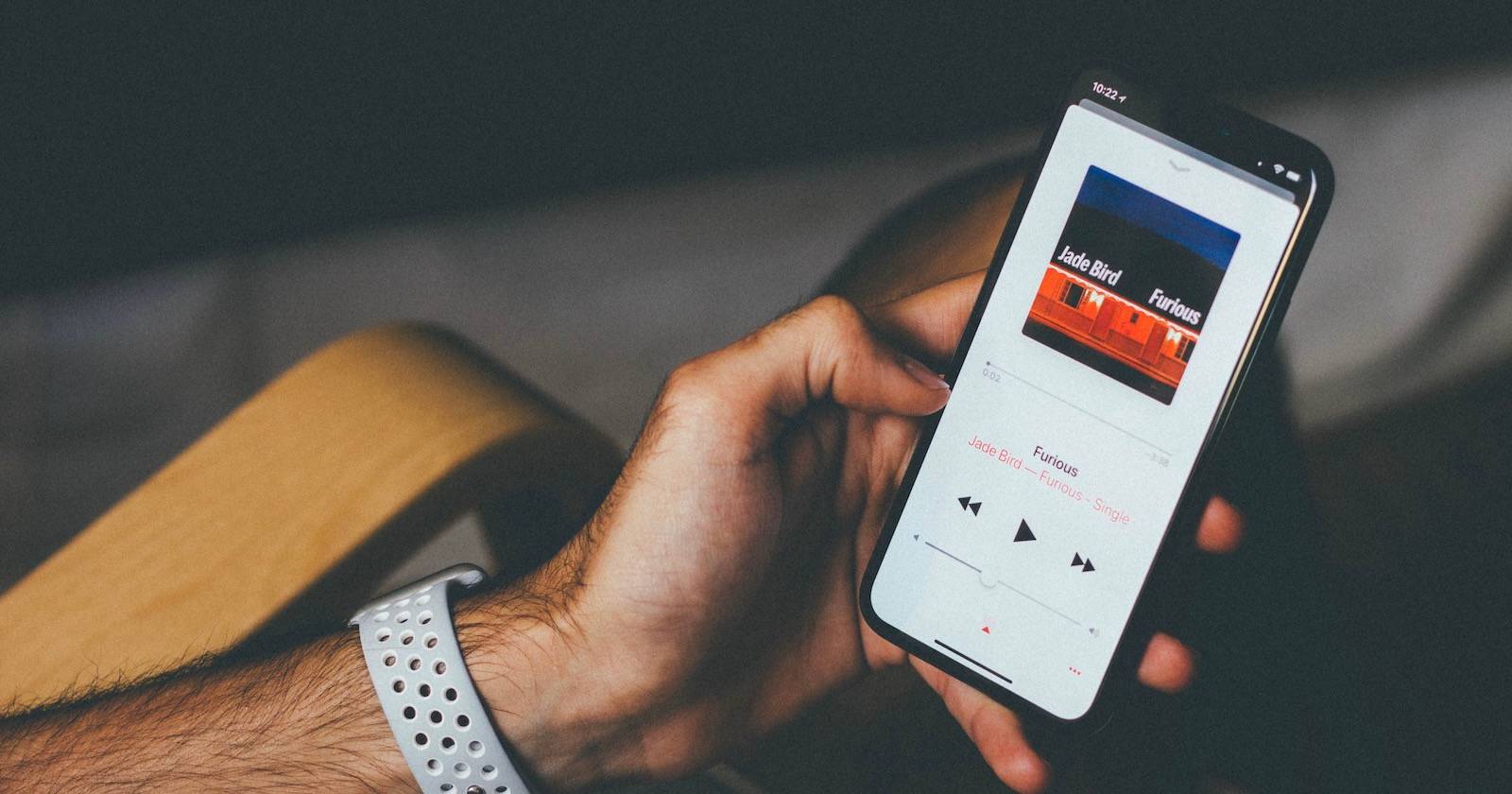 Рука держит iPhone с воспроизводимой песней в приложении «Музыка».
