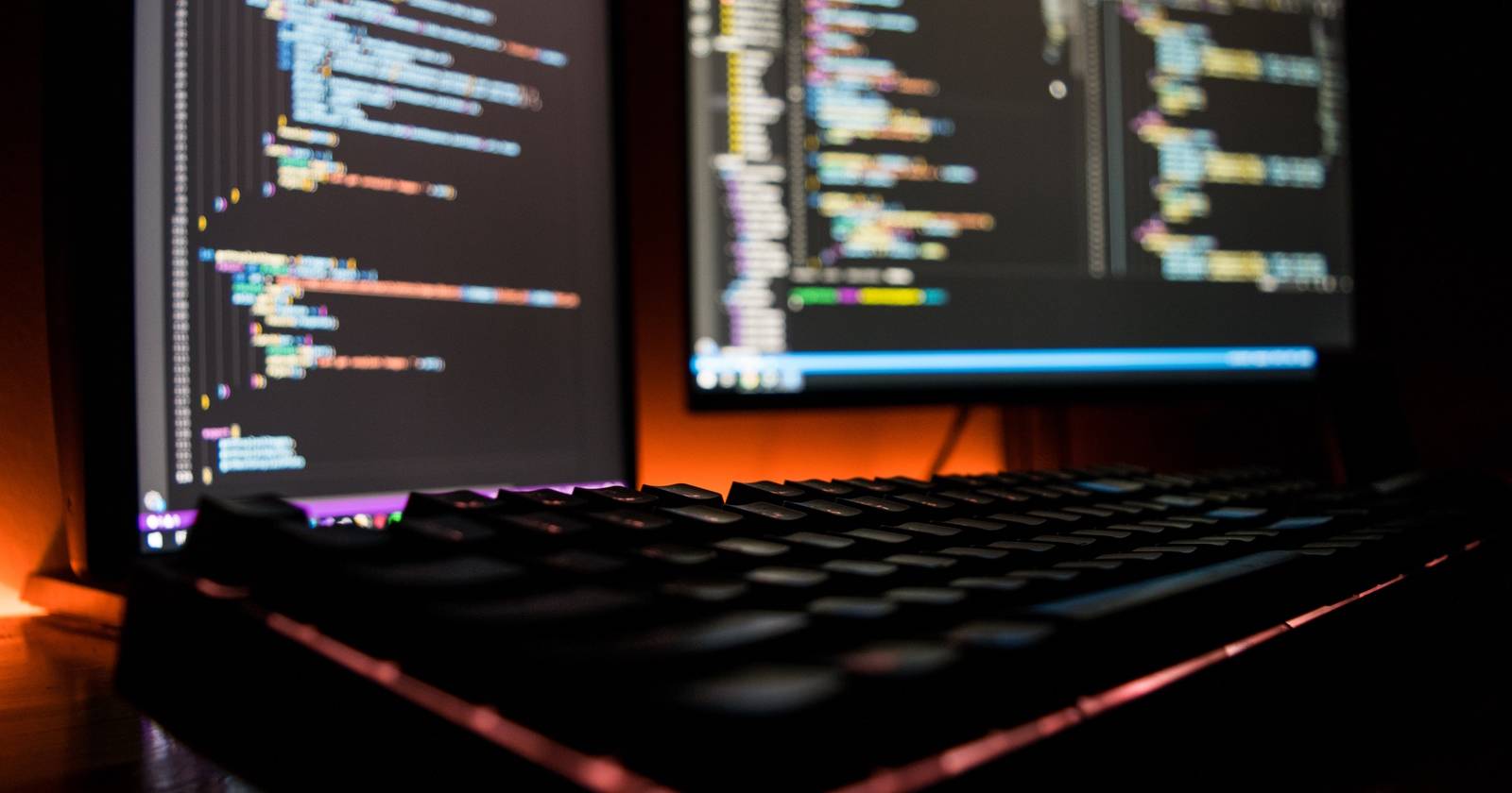 Компьютер на столе с двумя мониторами; на экранах виден код.