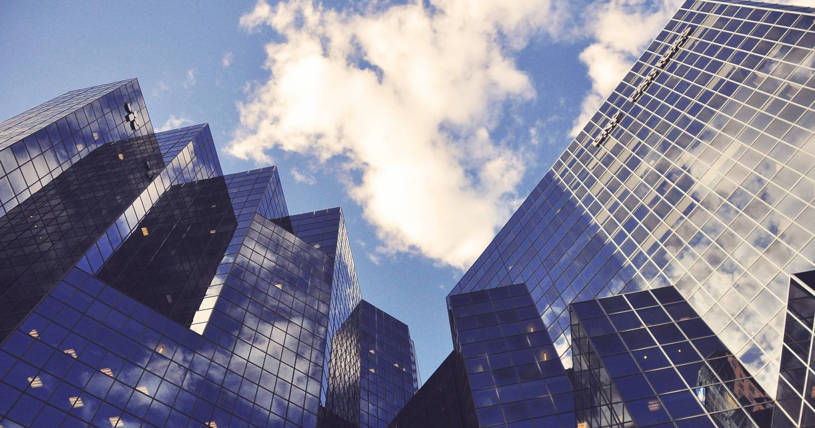 Несколько высоких небоскрёбов с остеклёнными фасадами, снятых с близкого расстояния у основания.