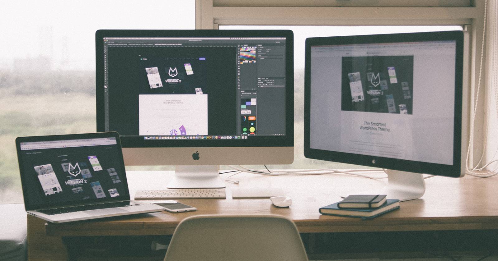 Ноутбук Mac на столе рядом с двумя внешними мониторами.