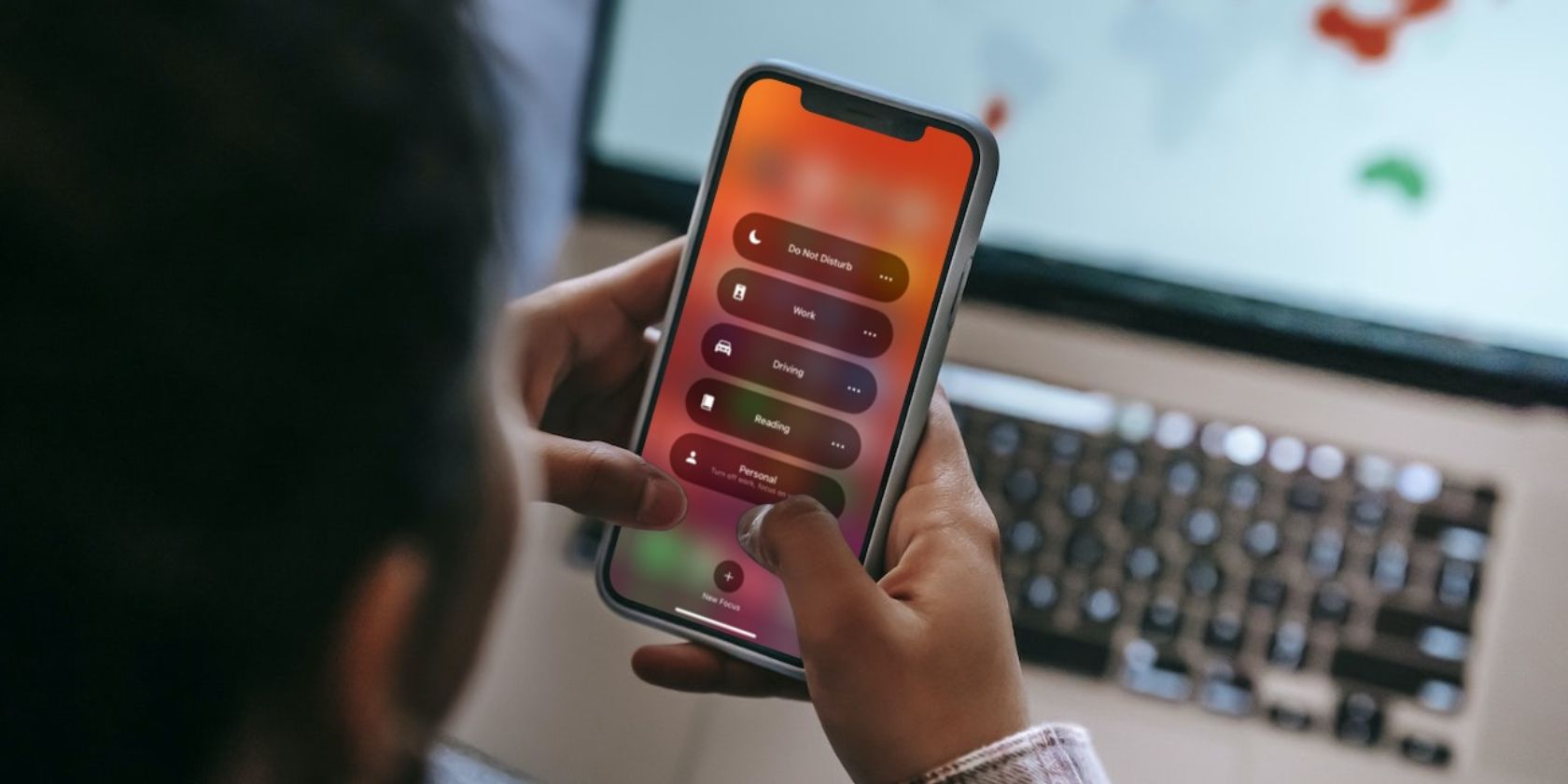Женщина использует iPhone с опциями Фокуса на экране, на заднем плане MacBook