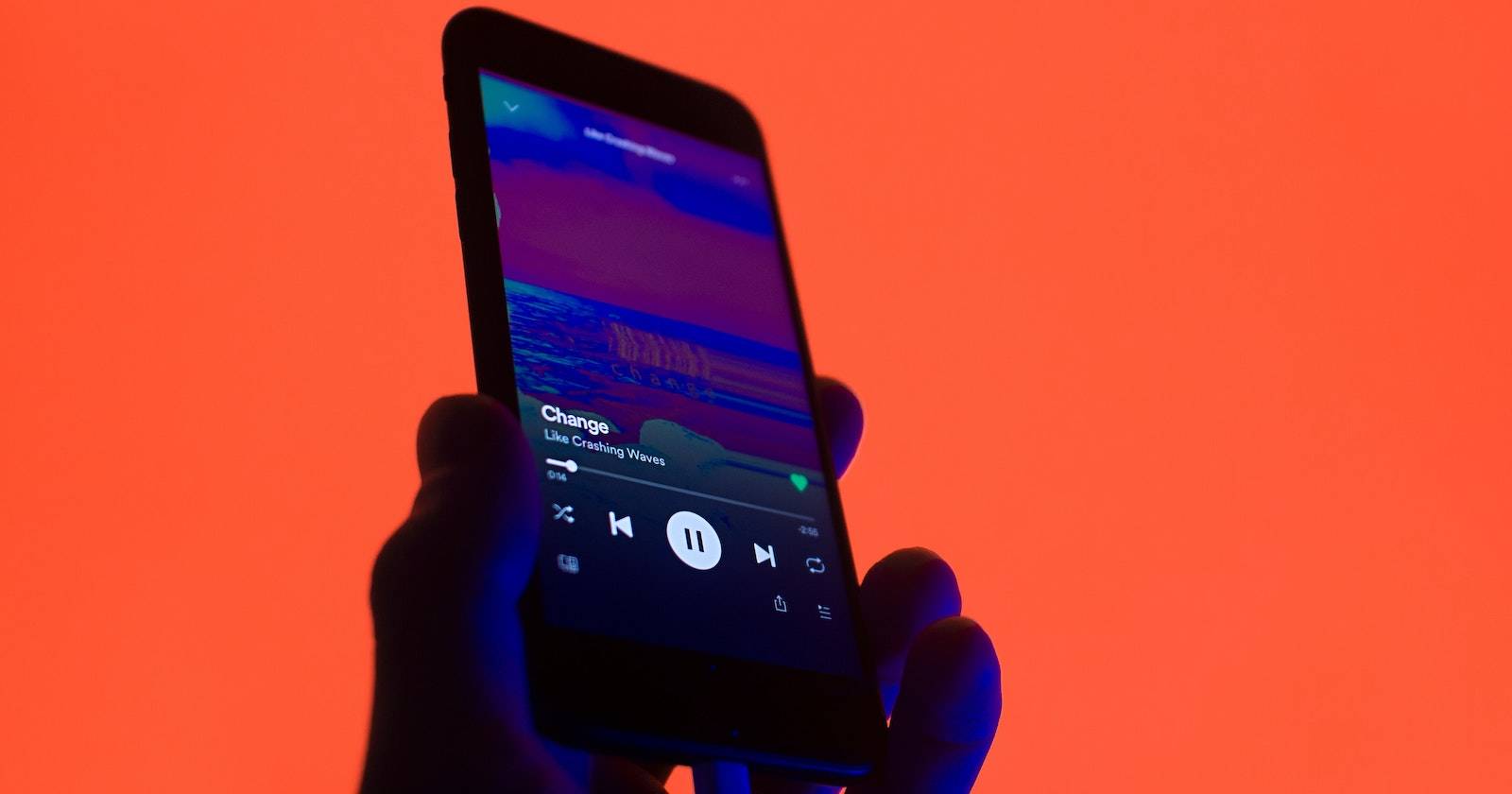 Человек держит телефон с приложением Spotify, экран с обложкой трека