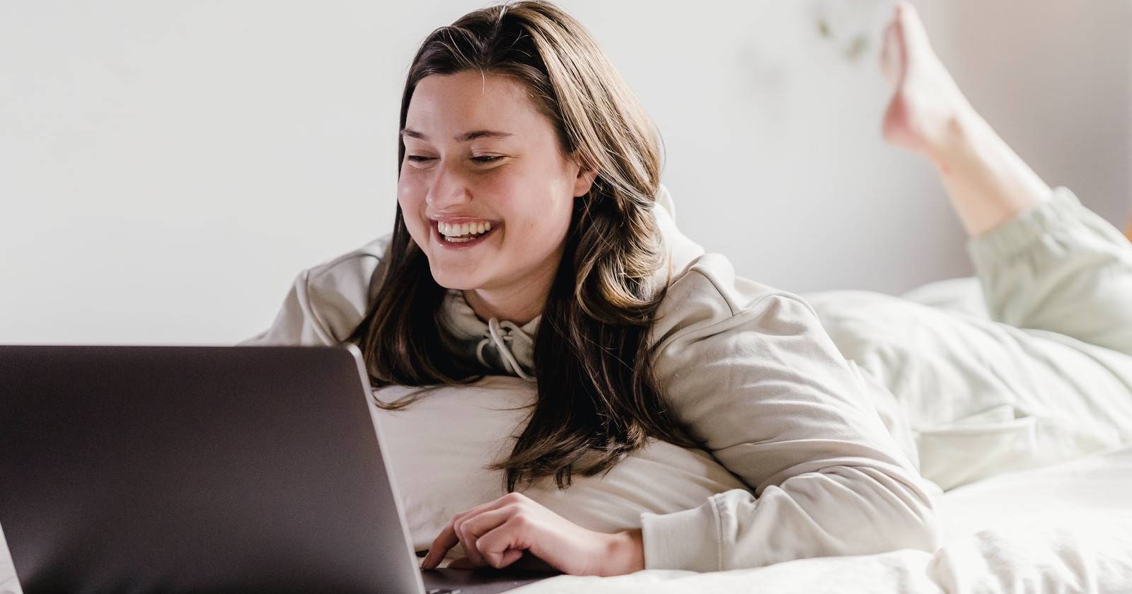 женщина радостно смотрит на ноутбук, лежа в кровати