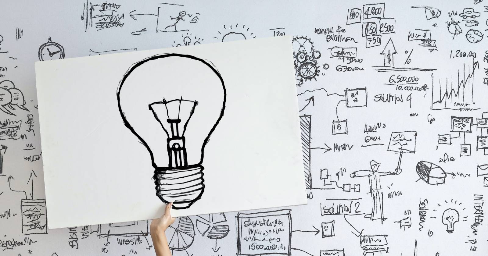 Рука держит лампочку на фоне схем и диаграмм на стене