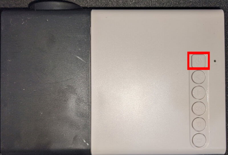 Фотография поверхности проектора с кнопкой питания и другими элементами управления.