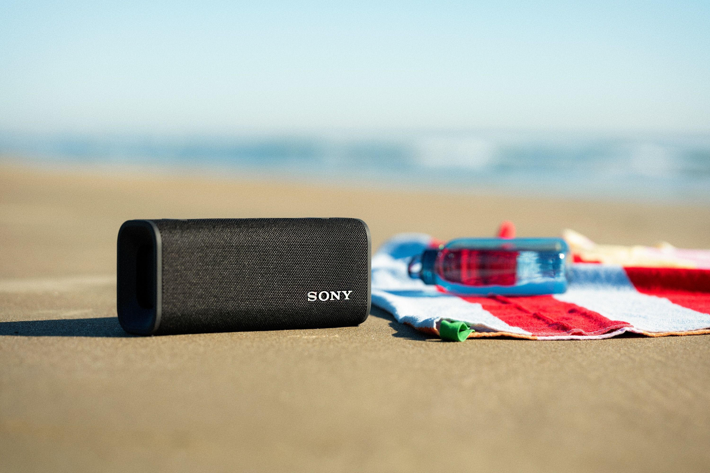 The Sony ULT Field 3on the beach next to a beach towel and water bottle.