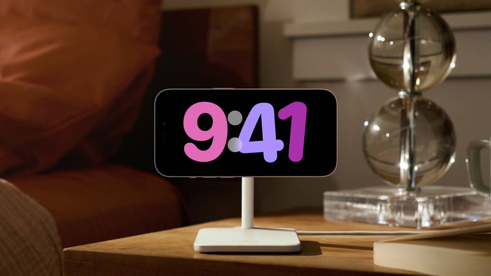 iPhone на тумбочке в режиме StandBy с цветными часами