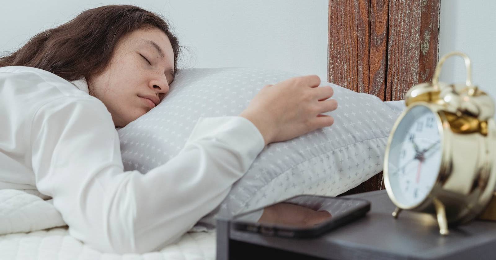 Человек спит рядом со смартфоном и настольными часами