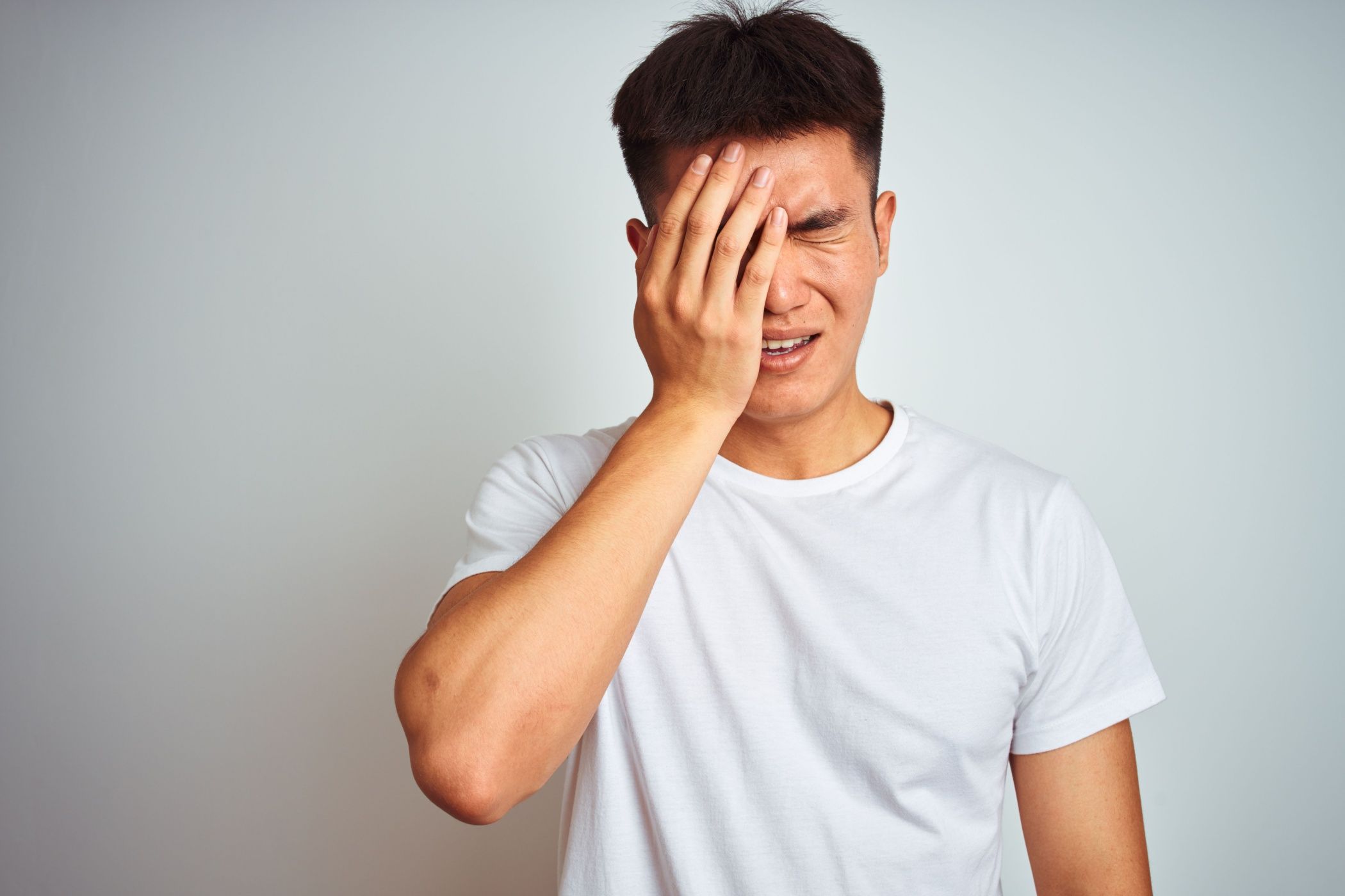 Молодой мужчина закрывает половину лица рукой после удара