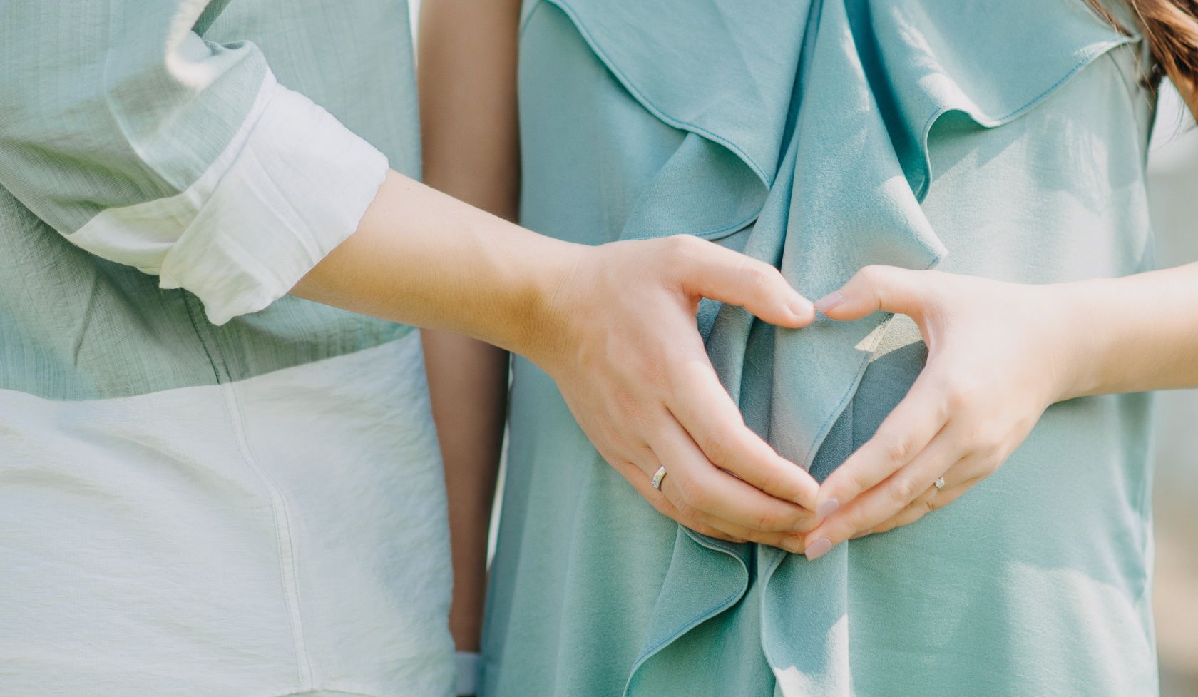 Пара образует сердечко руками над беременным животом