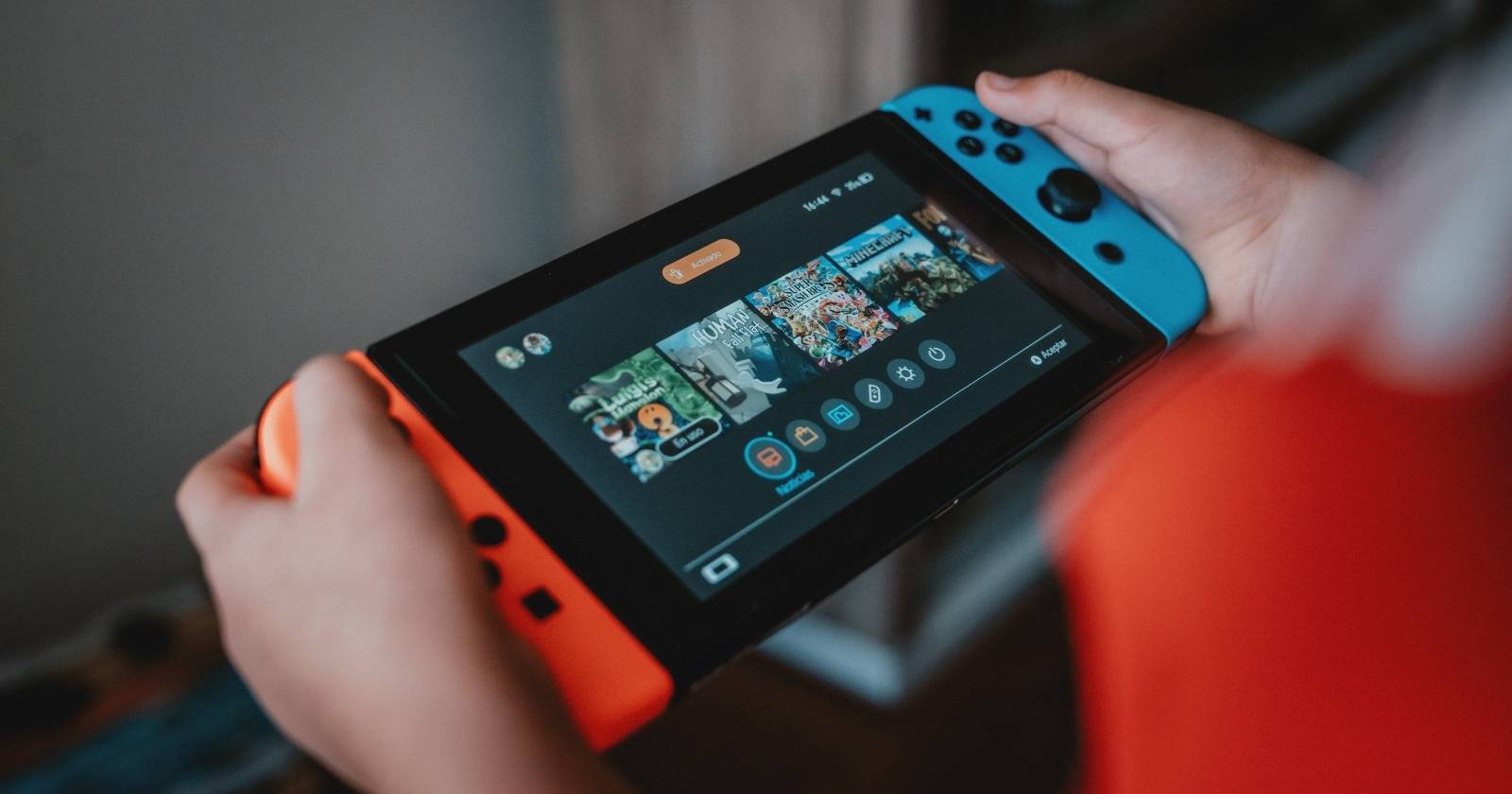 Фотография руки, держащей Nintendo Switch с выделенным приложением «Новости» на экране 