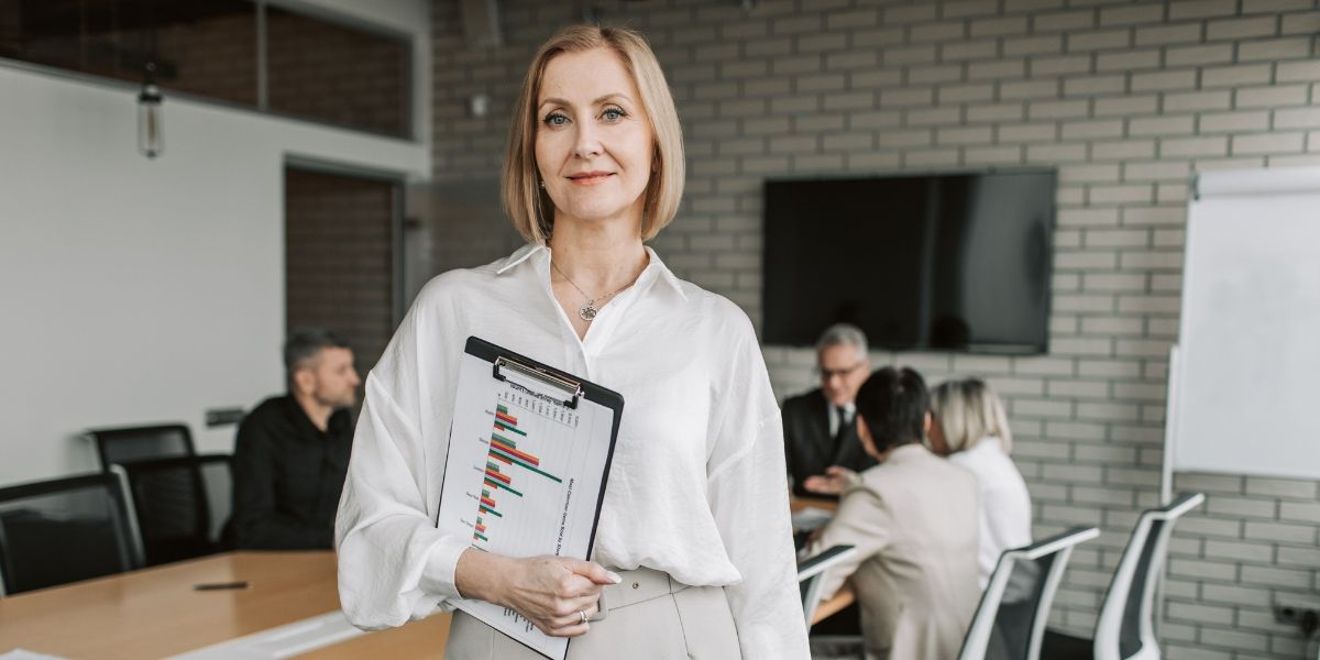 женщина в белой блузке улыбается и держит планшет на встрече