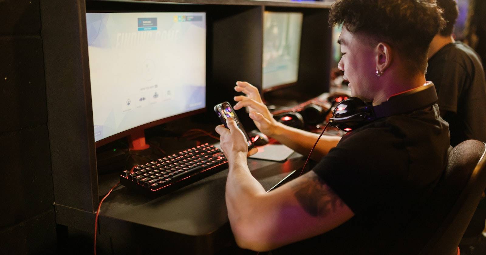 Человек в чёрной рубашке использует смартфон рядом с игровым компьютером
