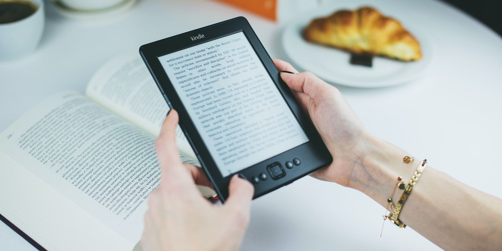 Человек держит устройство Kindle и читает в кафе