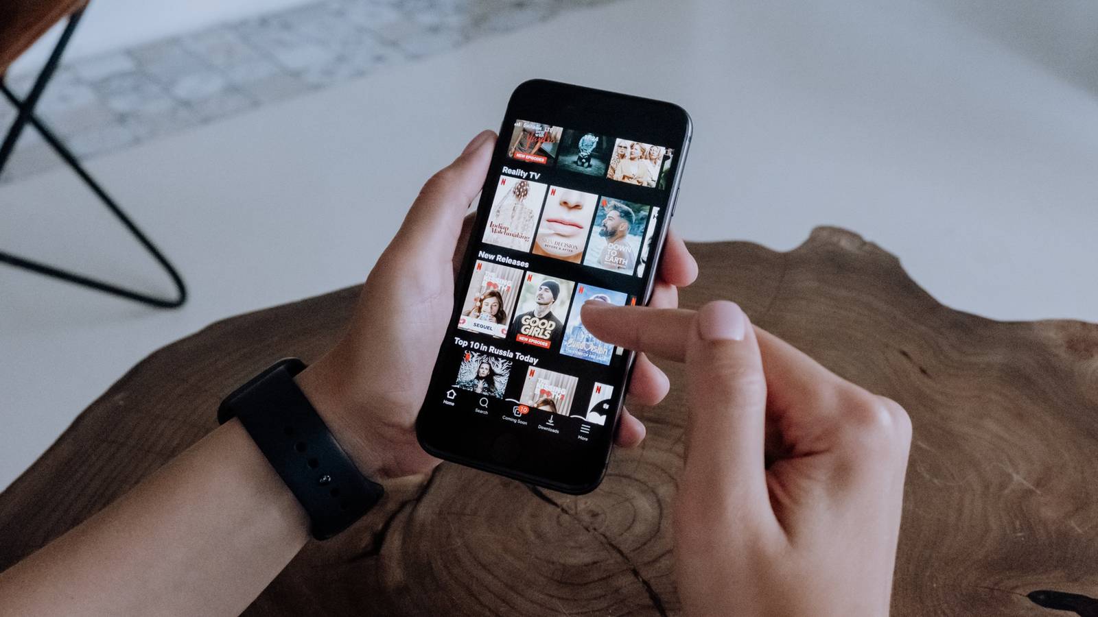 Человек держит чёрный смартфон и просматривает приложение Netflix