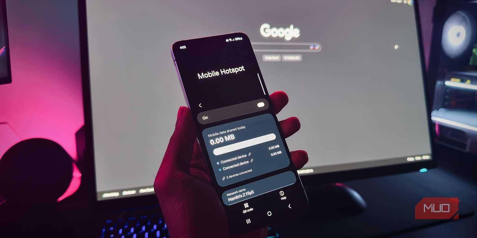 Рука держит Android‑телефон с включённой функцией «Точка доступа» на фоне монитора