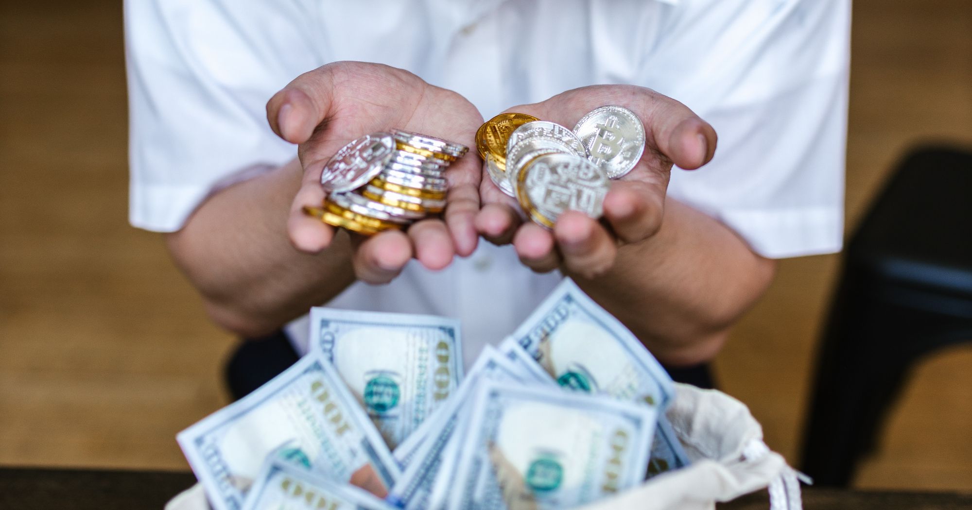 person holding bitcoins in hand behind sack of money